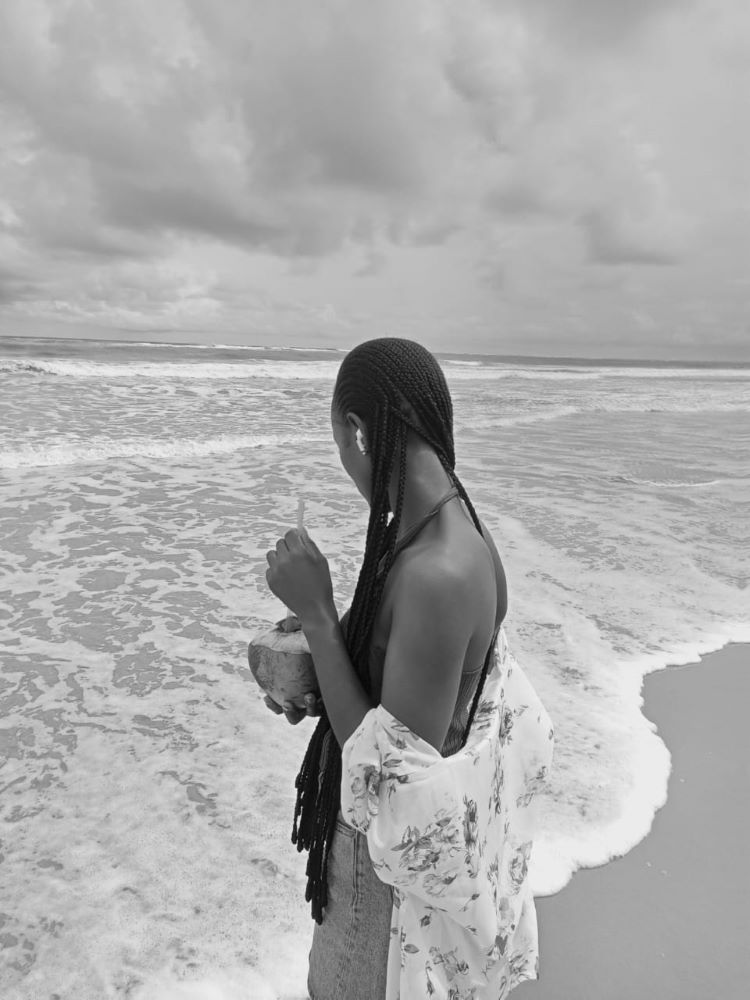 An image of me standing beside the Atlantic ocean passing throught Akwa-ibom state at Ibeno holding a coconut while admiring how beautiful nature can be